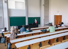 Mehrere Personen in einem Hörsaal, eine Person steht vorne, Präsentation sichtbar