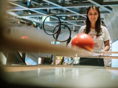 Junge Frau vor einer Konstruktion, Blick auf einen orangenen Ball gerichtet