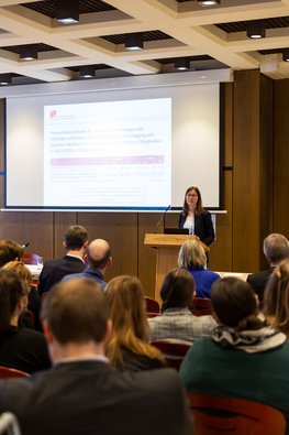 Eine Frau steht vor dem Publikum und hält eine Präsentation, Blick aus dem Publikum